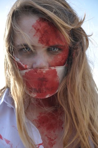 Blond woman covered in fake blood with a face mask